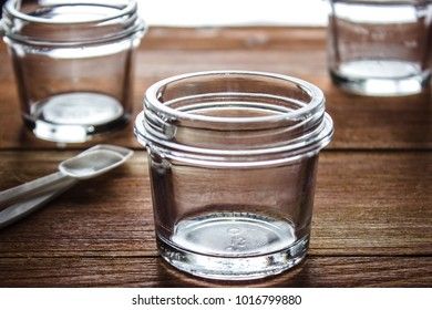 three small glass jars on a wooden background and two white spoons