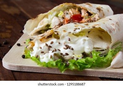 Shaurma chicken roll in a pita with fresh vegetables and cream sauce composition on wooden background