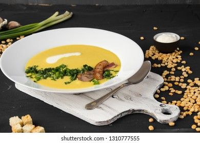 Pea soup with pieces of bacon, parsley and onion in a bowl on a dark background. Pea cream soup.