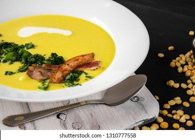 Pea soup with pieces of bacon, parsley and onion in a bowl on a dark background. Pea cream soup.