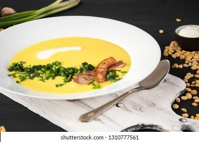 Pea soup with pieces of bacon, parsley and onion in a bowl on a dark background. Pea cream soup.