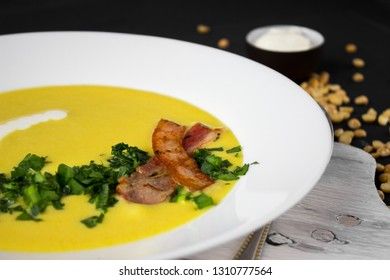 Pea soup with pieces of bacon, parsley and onion in a bowl on a dark background. Pea cream soup. Macro
