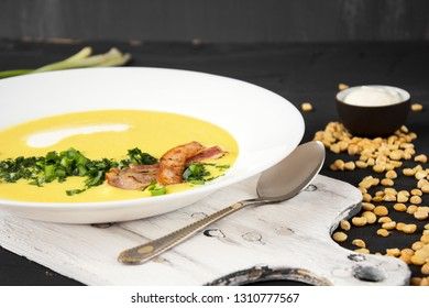Pea soup with pieces of bacon, parsley and onion in a bowl on a dark background. Pea cream soup.