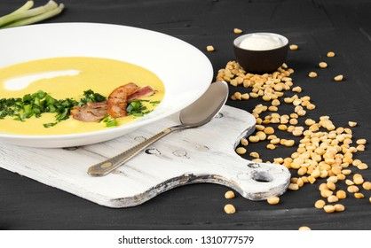 Pea soup with pieces of bacon, parsley and onion in a bowl on a dark background. Pea cream soup.