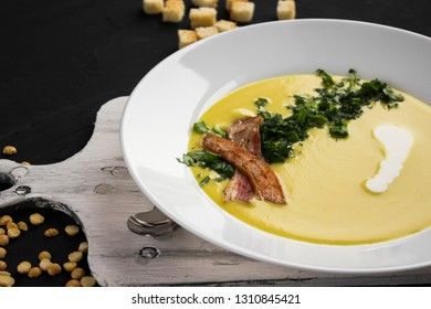 Pea soup with pieces of bacon, parsley and onion in a bowl on a dark background. Pea cream soup.