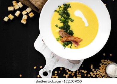 Pea soup with bacon and croutons on a dark background, top view. Yellow cream soup puree with greens.
