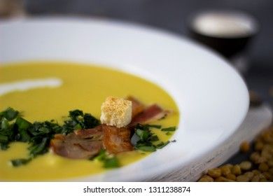 Pea soup with pieces of bacon, parsley and onion in a bowl on a dark background. Pea cream soup. Macro.