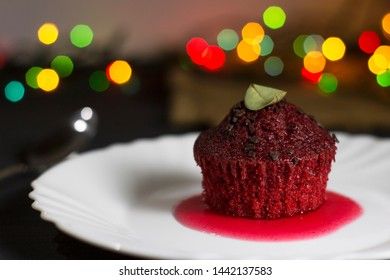 Red cupcake with chocolate chips on a dark background with multi-colored bokeh